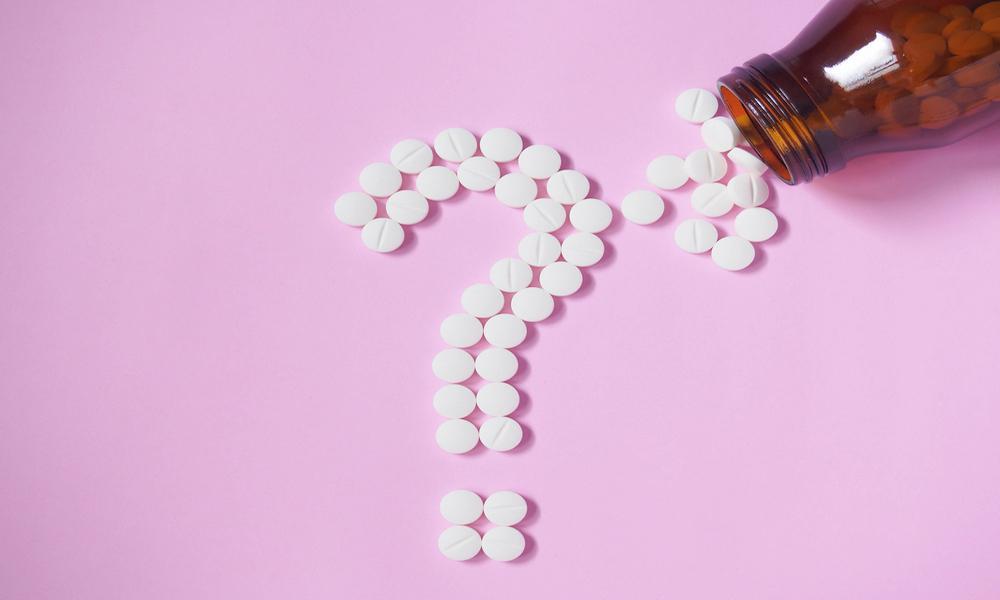 pills in a question mark shape on a pink table